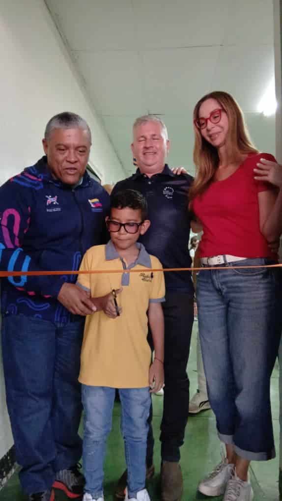 El niño Andrés con anteojos y polo amarilla cortando la cinta naranja inaugural escoltado por 3 adultos.